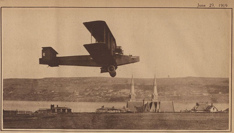 Biplane flying over Harbour Grace with church spires in the background