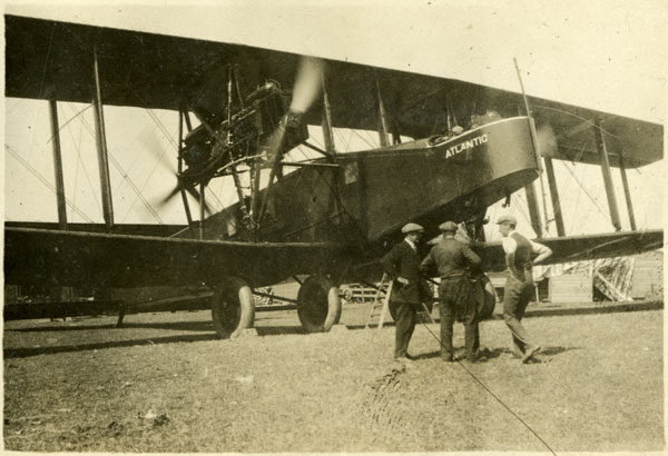 Three men standing in front of the biplane Atlantic. The propellers are spinning and blurred in the picture.