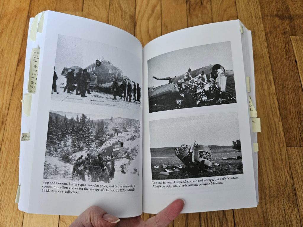 A book open to a page with four black and white photos of different plane crashes. Small strips of yellow sticky notes are sticking out from the other pages of the book, many with writing visitble.