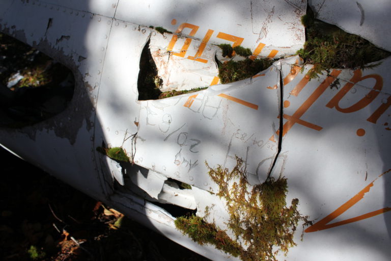 A fragmented piece of airplane aluminum with the word Aviation Ltd painted in orange on the site. Some graffiti has been scratched into the paint.