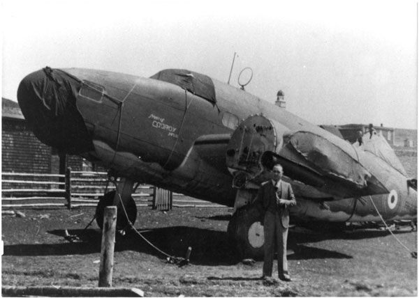 Black and white photo of Magistrate Jack Dawson stands in front of salvaged aircraft. Note "Spirit of Codroy NFLD." painted on the nose. The wings and engines are missing from the aircraft, and the nose cone and cockpit are covered with tarpaulins.